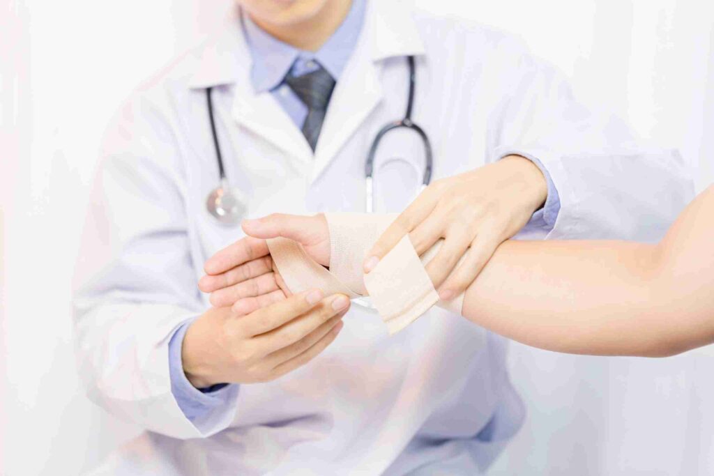 Male doctor putting gauze on young man's hand in clinic, closeup