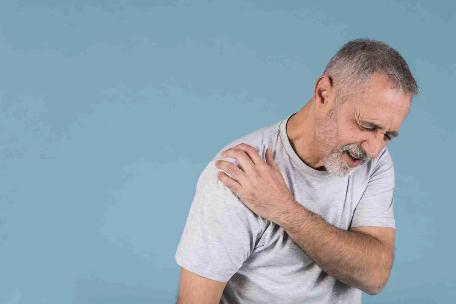 stressed senior man with shoulder pain blue backdrop
